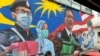 FILE - A Malay couple have lunch next to a graffiti tribute to Malaysian workers on the frontlines against the COVID-19 coronavirus at Damansara in Selangor, outside Kuala Lumpur, Malaysia, Nov. 7, 2020. 