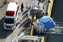 Officers in protective gear escort a person (under the blue sheet) who was on board cruise ship Diamond Princess and was tested positive for coronavirus, in Yokohama, south of Tokyo in this photo taken by Kyodo, Feb. 4, 2020.