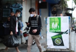People walk by a poster reading in Vietnamese "Fighting COVID-19" in Hanoi, Vietnam on Thursday, Apr. 23, 2020. Business activities resume in Vietnam as the country lifts the nationwide lockdown to contain the spread of COVID-19.