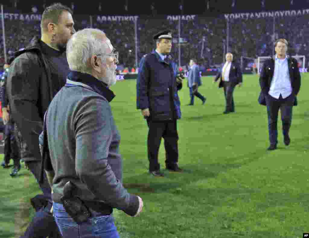 Mai kungiyar PAOK, Ivan Savvidis, rataye da bindiga a kunkuminsa, tare da masu gadinsa, a lokacin da ya kutsa cikin filin wasa a karawarsu da AEK Athens ranar lahadai a birnin&nbsp; Thessaloniki. Sau biyu Savvidis yana kutsawa cikin filin a lokacin wasa. Jami&#39;an AEK sun yi zargin cewa Savvidis yayi barazana ga alkalin wasan a kutsawarsa ta farko, kafin masu gadinsa su janye shi. A karo na biyu an ga bindiga a rataye a kunkuminsa.(InTime Sports via AP)
