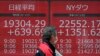 A man walks past an electronic stock board showing Japan's Nikkei 225 and New York Dow Jones index, at a securities firm in Tokyo, Japan, March 27, 2020.