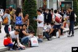 中國遊客在日本東京銀座購物後坐在路牙子上休息。（2015年5月6日）