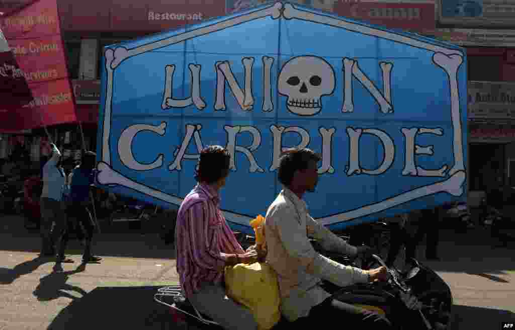 Indian motorists drive past a poster bearing the name of the Union carbide company during a march by Bhopal Gas disaster victims to commemorate the 30th anniversary in Bhopal, Dec. 3, 2014. 