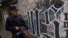 FILE - A member of the Salvadoran National Police walks next to symbol of the "Mara Salvatrucha" gang painted on a wall during an anti-gang operative in San Salvador, El Salvador.