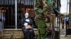 FILE - An armed police officer walks past an environmental protester wearing a skeleton costume as she demonstrates outside parliament against recent government plans to mine coal and open a coal-fired power plant, in downtown Nairobi, Kenya, June 5, 2018. 